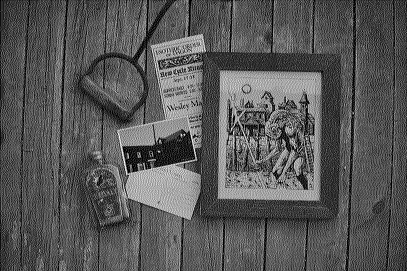 Photo of a print of the illustration alongside a pamhplet and a postcard of the town, a bottle of whiskey and a hook